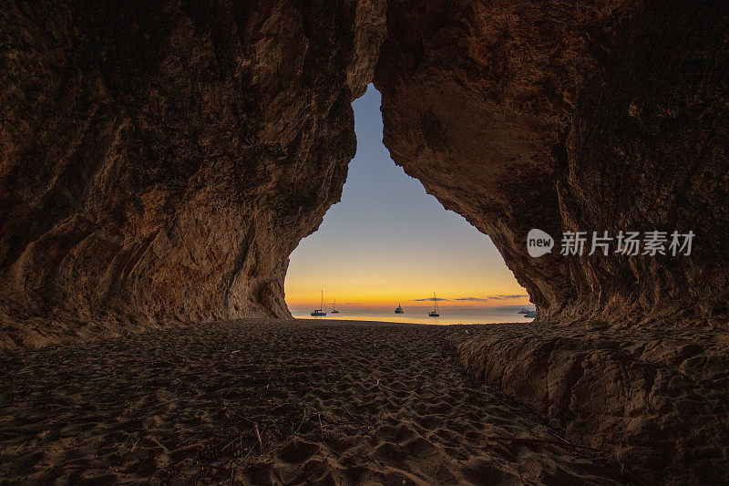 意大利撒丁岛的奥罗塞湾，Cala Luna洞穴，夕阳下，背景是帆船。